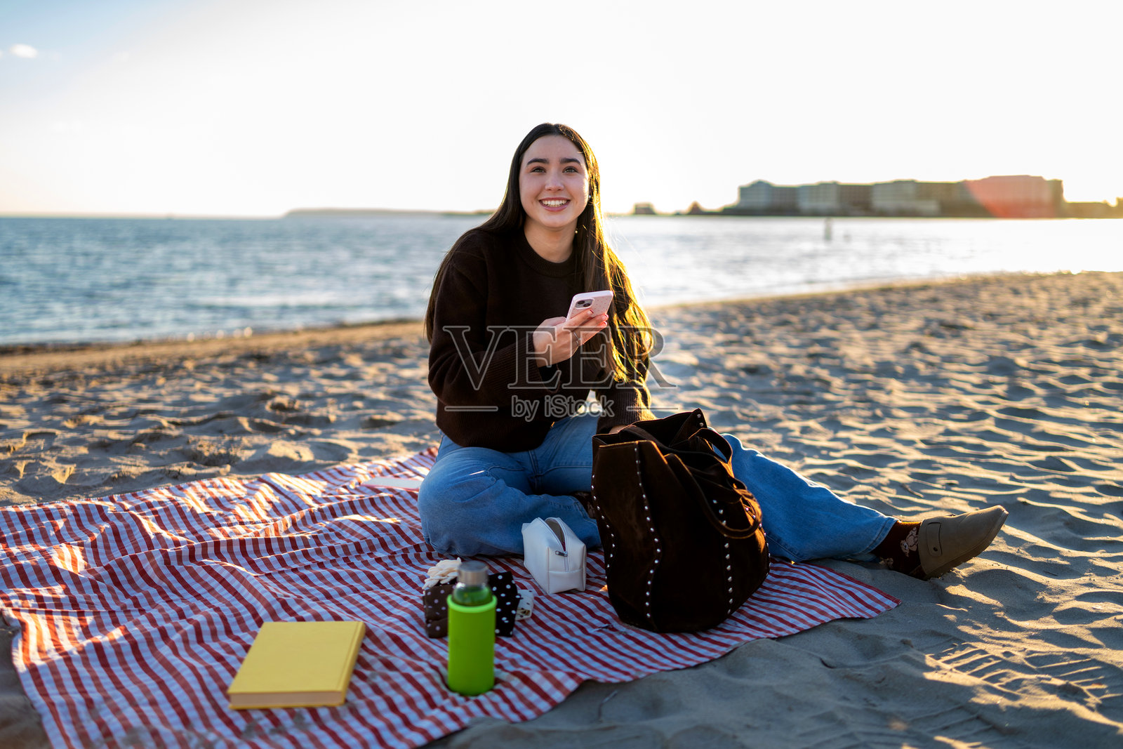 年轻女子在舒适的海滩上享受时光,并使用智能手机照片摄影图片