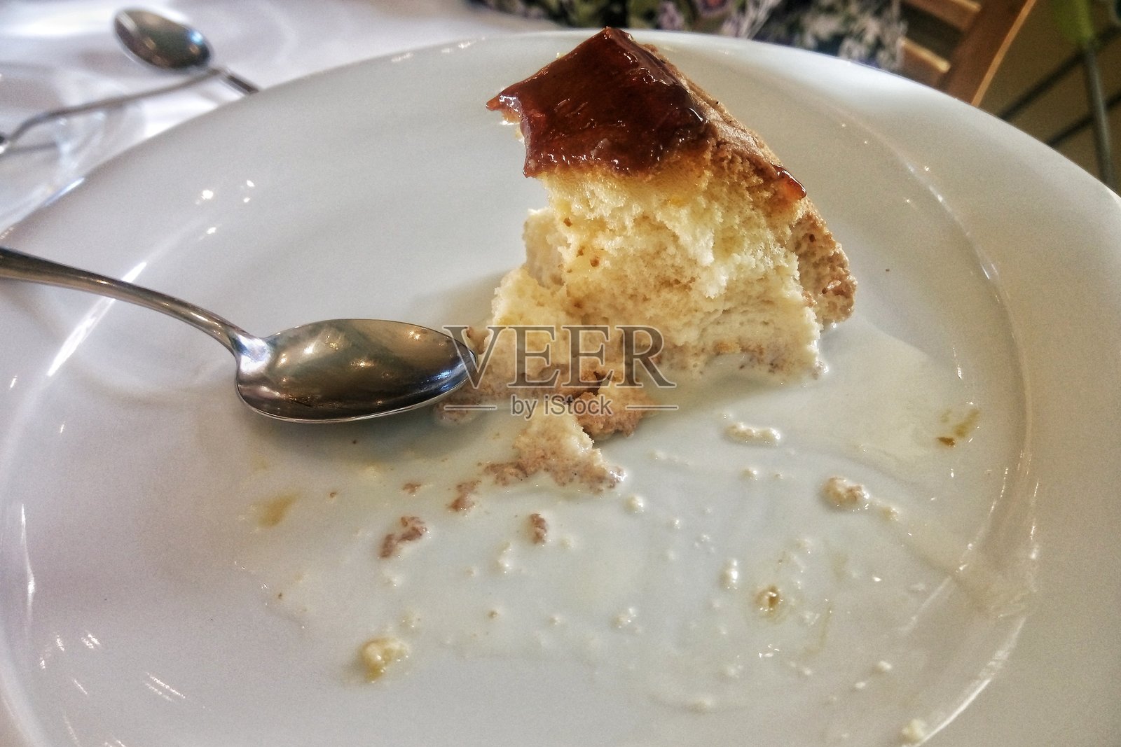 一块被吃了一半的软焦糖蛋糕,很可能是受欢迎的“三奶蛋糕”甜点,配有额外的牛奶酱和一把金属勺子,盛放在一个纯白色的陶瓷盘中照片摄影图片