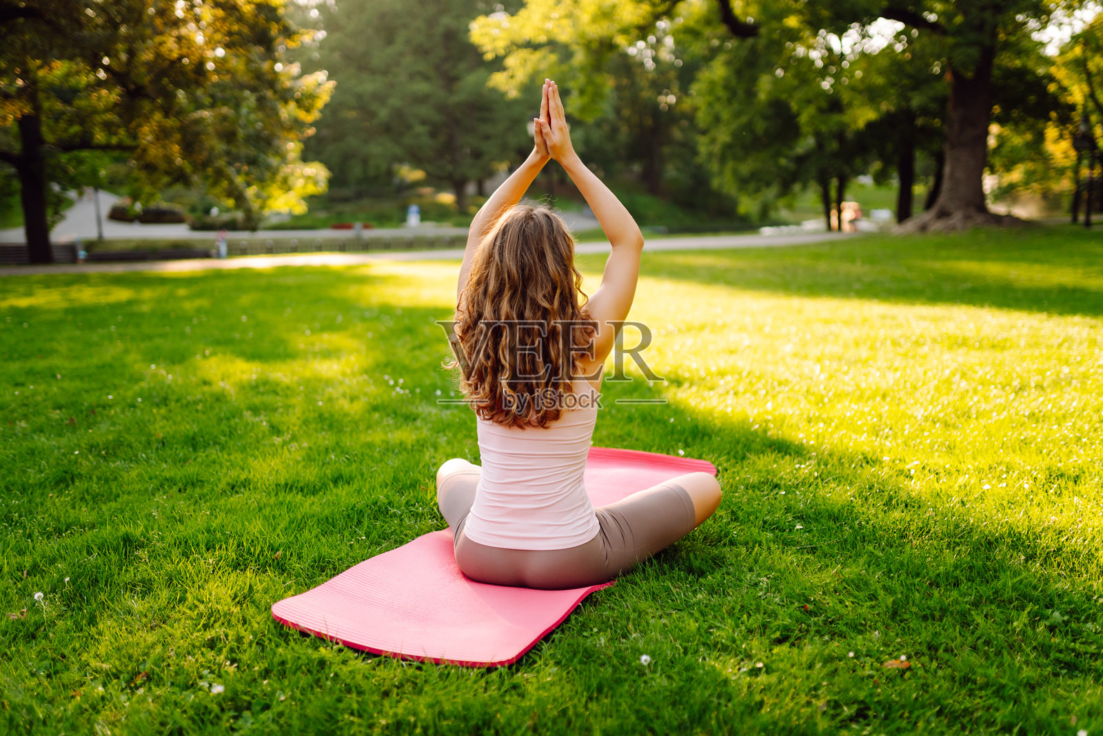 一位快乐的女士在阳光明媚的公园里,在瑜伽垫上练习瑜伽。照片摄影图片