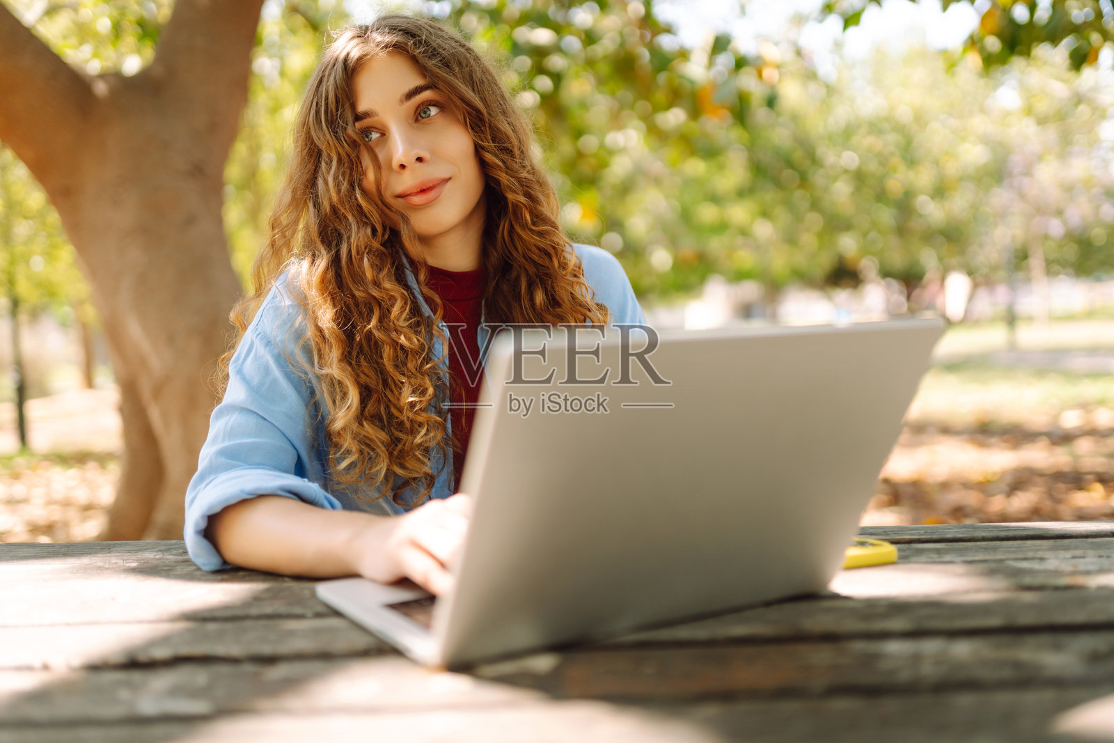 一位微笑的女士坐在公园的桌子旁,使用笔记本电脑工作。照片摄影图片