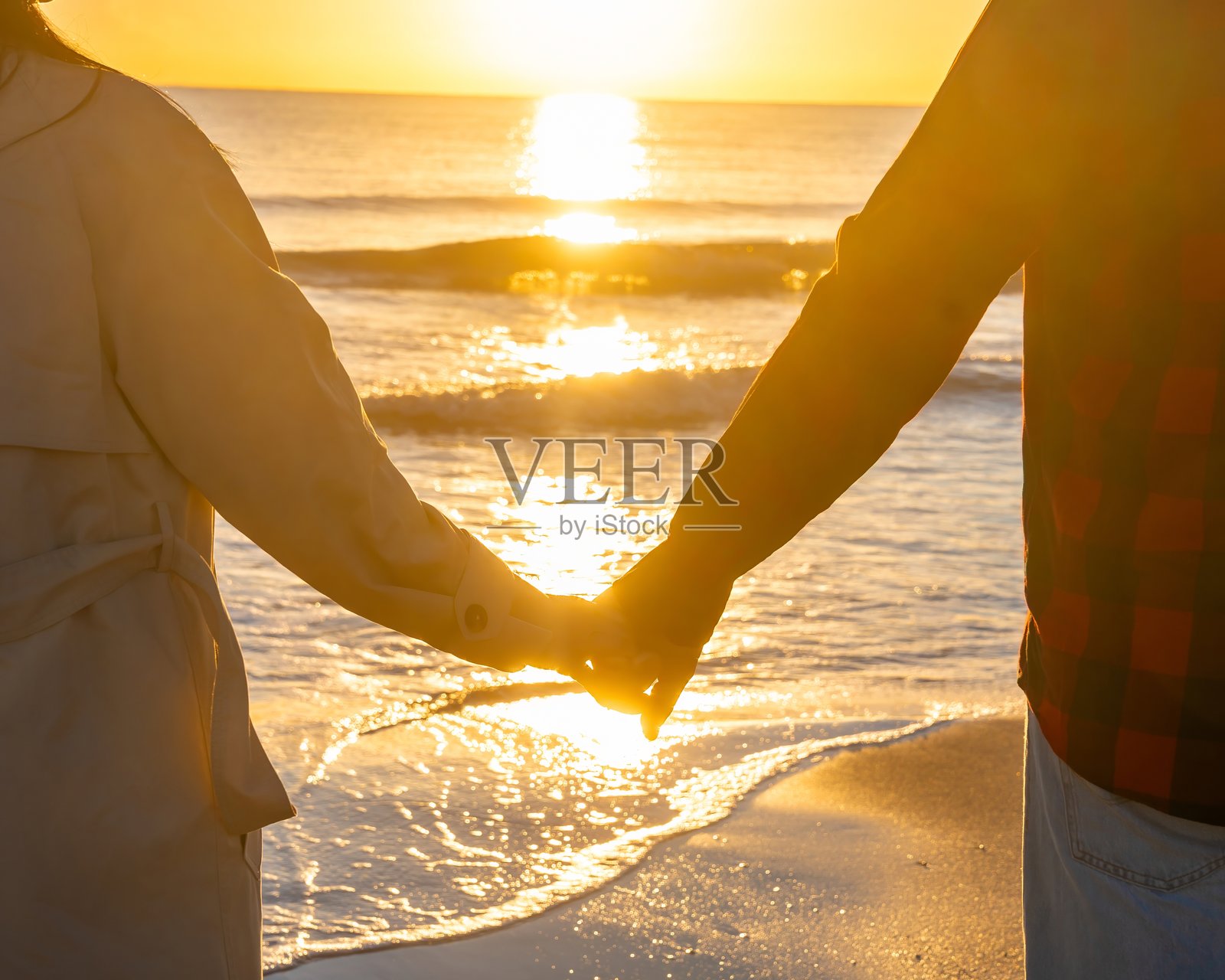 情侣在夕阳余晖中漫步,伴侣们手牵手,在轻柔的海浪和温暖的光线下,享受着宁静的海滨日落散步照片摄影图片