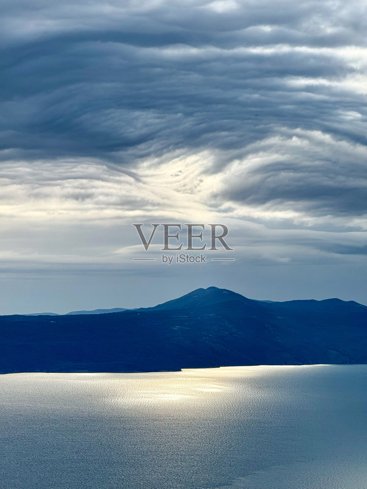 剪影:岛屿上空乌云密布,海面波光粼粼照片摄影图片