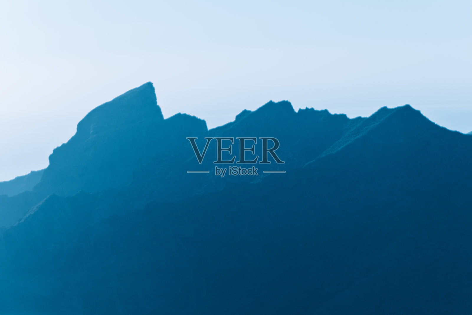 锯齿状山峰的剪影在渐变蓝天下升起照片摄影图片