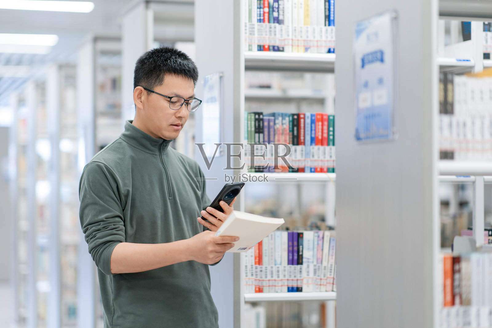 图书馆内男子手持手机阅读书籍照片摄影图片