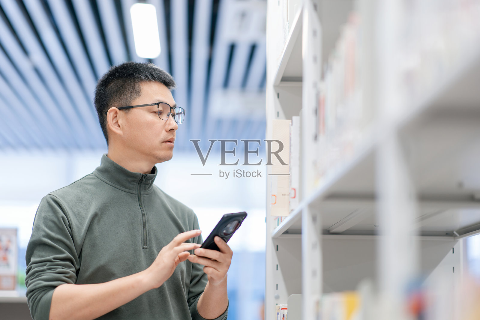 戴眼镜男子图书馆查手机选书照片摄影图片