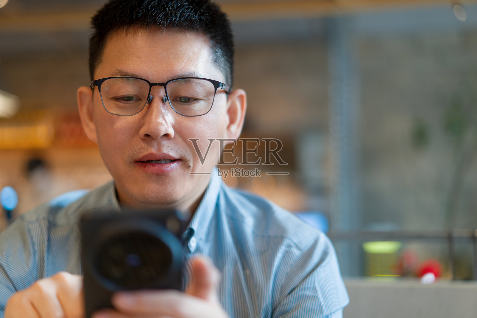 戴眼镜男子手持手机专注拍摄照片摄影图片