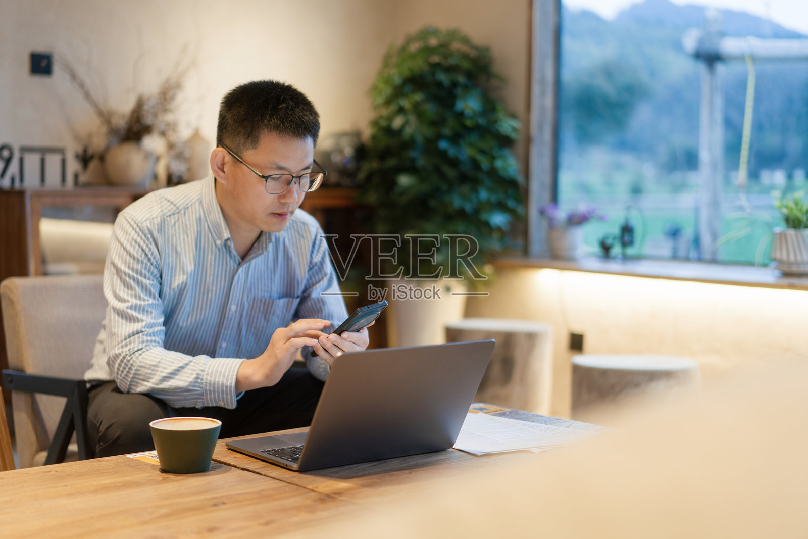 戴眼镜男子室内用手机看笔记本电脑照片摄影图片