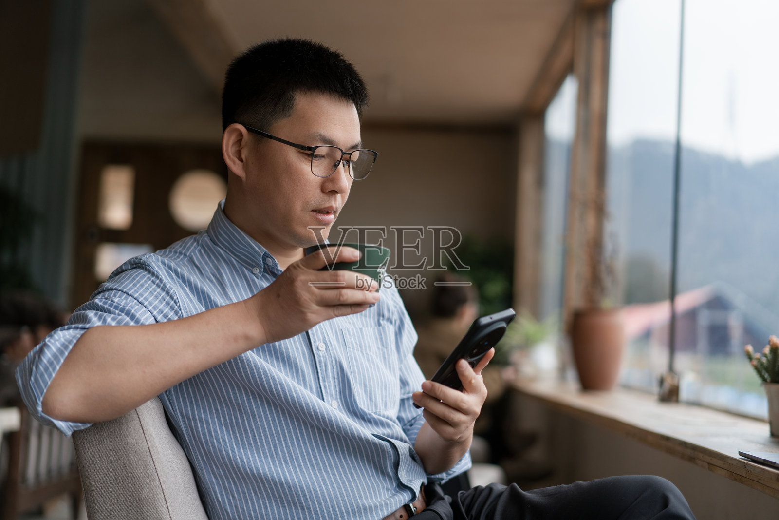 戴眼镜男子咖啡馆看手机喝咖啡照片摄影图片