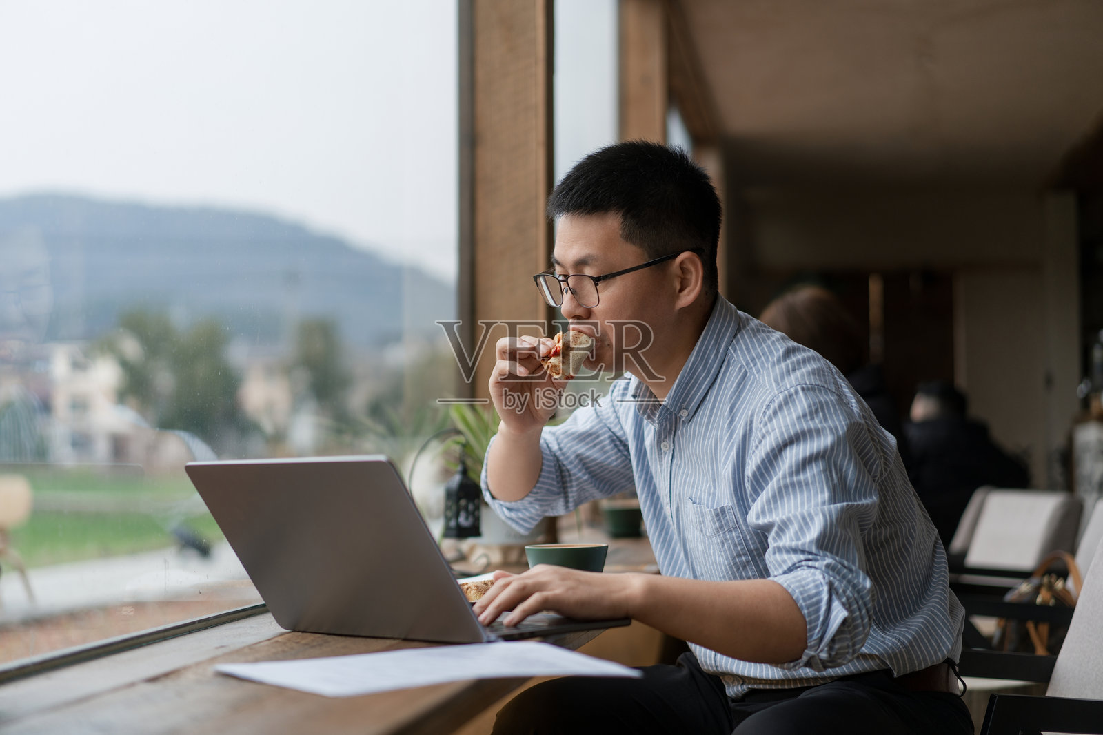 戴眼镜男子窗边用笔记本吃披萨照片摄影图片