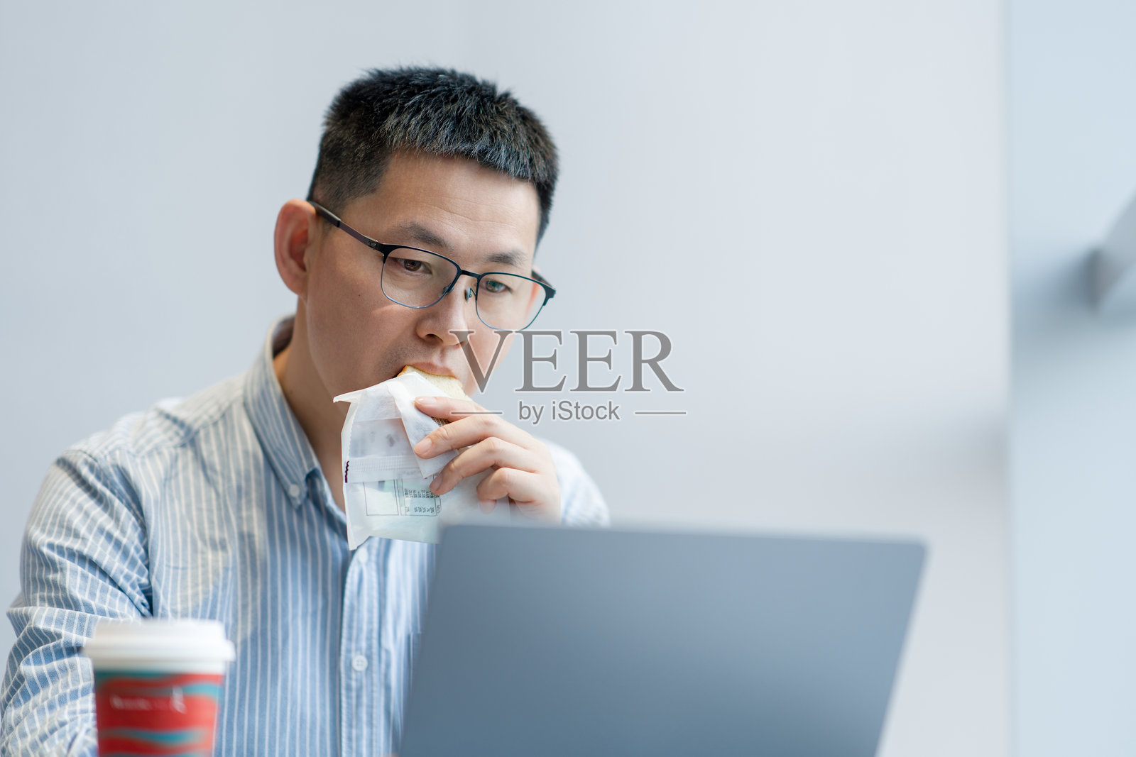 戴眼镜男子办公室吃早餐用笔记本电脑照片摄影图片