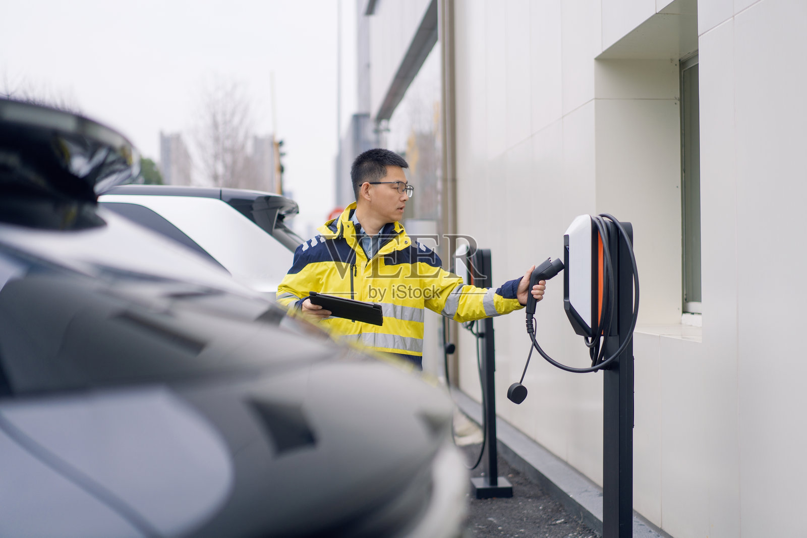 穿黄反光服男子插电桩为电动车充电照片摄影图片