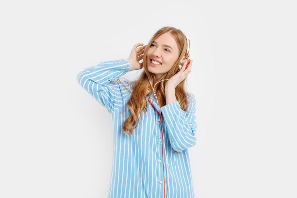 快乐迷人的年轻女孩穿着睡衣在白色背景上用耳机听音乐图片 快乐迷人的年轻女孩穿着睡衣在白色背景上用耳机听音乐图片下载