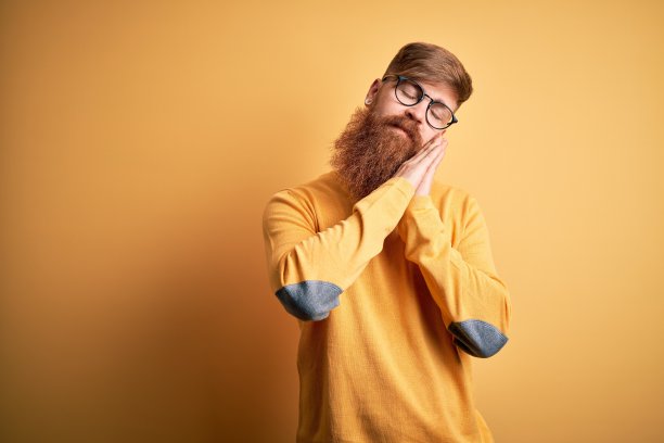 英俊的爱尔兰红发男子与胡子戴眼镜在黄色孤立的背景睡累了,做梦,摆姿势与手在一起,而闭上眼睛微笑。图片 英俊的爱尔兰红发男子与胡子戴眼镜在黄色孤立的背景睡累了,做梦,摆姿势与手在一起,而闭上眼睛微笑。图片下载