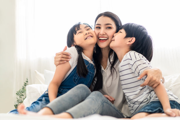 亚洲母亲,儿子和女儿坐在白色的床上幸福和微笑的卧室。妈妈抱着男孩和女孩一起玩。孩子们在温暖的房子里用爱亲吻妈妈。幸福的家庭关系。图片 亚洲母亲,儿子和女儿坐在白色的床上幸福和微笑的卧室。妈妈抱着男孩和女孩一起玩。孩子们在温暖的房子里用爱亲吻妈妈。幸福的家庭关系。图片下载