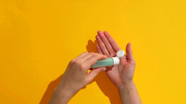 一个女人的手正在用一个凝胶瓶在黄色的背景图片 一个女人的手正在用一个凝胶瓶在黄色的背景图片下载