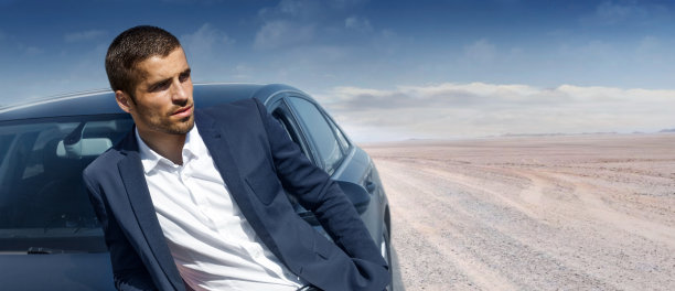 一个男人,一个英俊的司机倚在一辆汽车的引擎盖上,在夏天的沙路上图片 一个男人,一个英俊的司机倚在一辆汽车的引擎盖上,在夏天的沙路上图片下载