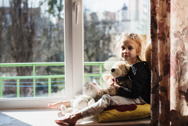 可爱的小女孩坐在窗前享受阳光。孩子坐在大窗台上玩。维生素D图片 可爱的小女孩坐在窗前享受阳光。孩子坐在大窗台上玩。维生素D图片下载