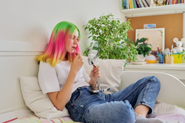 十几岁的女孩坐在家里的床上,用化妆镜给她的嘴唇涂上唇彩图片 十几岁的女孩坐在家里的床上,用化妆镜给她的嘴唇涂上唇彩图片下载
