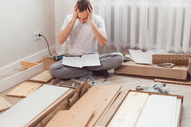 困惑的男人在家里组装新的木制家具。男人看了说明书而误解了下一步该做什么。图片 困惑的男人在家里组装新的木制家具。男人看了说明书而误解了下一步该做什么。图片下载