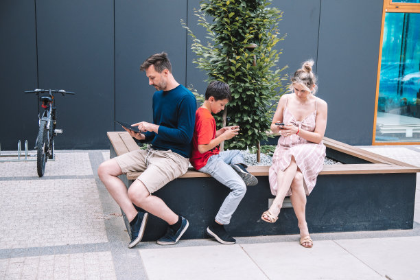 夏日,年轻的家庭在城市广场上使用平板电脑、智能手机。技术概念图片 夏日,年轻的家庭在城市广场上使用平板电脑、智能手机。技术概念图片下载