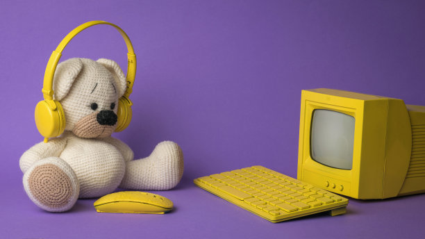 紫色背景下的黄色电脑前有一只针织熊。图片 紫色背景下的黄色电脑前有一只针织熊。图片下载