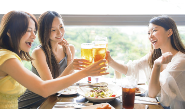 快乐的年轻女性朋友在餐馆里碰杯喝啤酒图片 快乐的年轻女性朋友在餐馆里碰杯喝啤酒图片下载