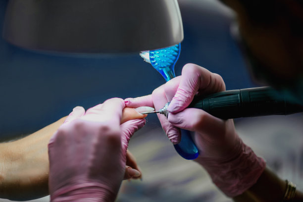 一名女子在美容院使用电动指甲锉钻。特写指甲修剪过程与飞的碎片。图片 一名女子在美容院使用电动指甲锉钻。特写指甲修剪过程与飞的碎片。图片下载