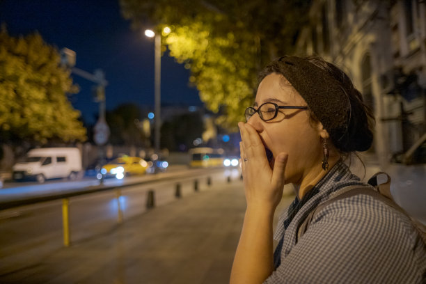 晚上,疲倦的年轻女子在外面等公共汽车时打呵欠图片 晚上,疲倦的年轻女子在外面等公共汽车时打呵欠图片下载
