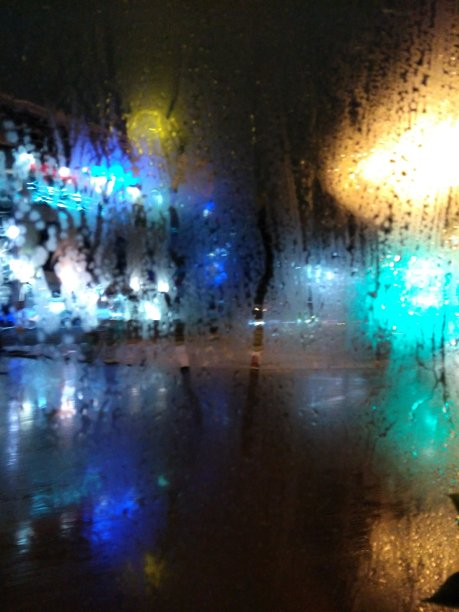 明亮的彩光透过雾蒙蒙的玻璃。下雨了。滴在玻璃上。城市夜晚的背景。图片 明亮的彩光透过雾蒙蒙的玻璃。下雨了。滴在玻璃上。城市夜晚的背景。图片下载