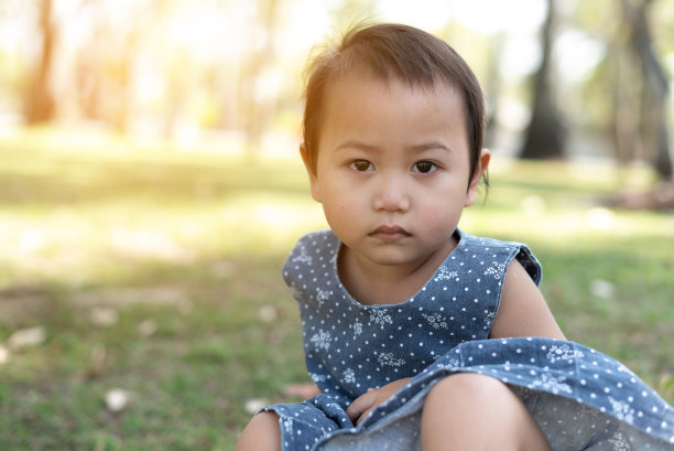 年轻的亚洲小孩坐在户外公园的草地上,沮丧和担心的痛苦,哭愤怒和害怕。悲伤的表情。图片 年轻的亚洲小孩坐在户外公园的草地上,沮丧和担心的痛苦,哭愤怒和害怕。悲伤的表情。图片下载