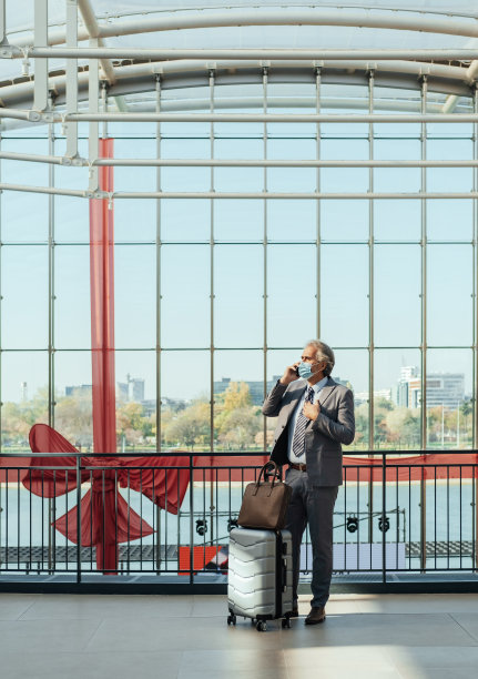 一个拎着行李箱的商人站在机场候机楼边打电话图片 一个拎着行李箱的商人站在机场候机楼边打电话图片下载