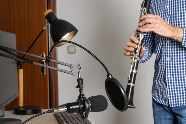 年轻的企业家在家里吹单簧管,用电脑录制音乐并在线播放图片 年轻的企业家在家里吹单簧管,用电脑录制音乐并在线播放图片下载