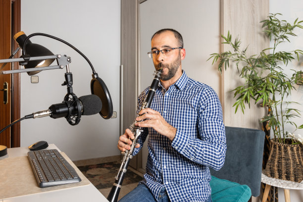 年轻的企业家在家里吹单簧管,用电脑录制音乐并在线播放图片 年轻的企业家在家里吹单簧管,用电脑录制音乐并在线播放图片下载