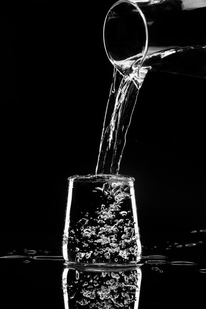 水在黑色的背景下从玻璃瓶中倒入玻璃杯图片 水在黑色的背景下从玻璃瓶中倒入玻璃杯图片下载