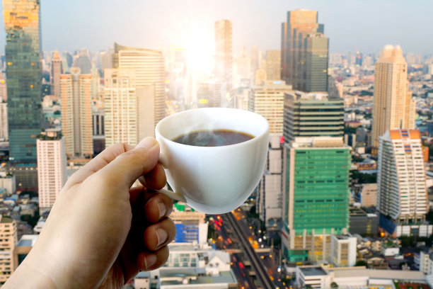 一个男人的手拿着一个热咖啡杯与烟在新的早晨在现代城市的背景图片 一个男人的手拿着一个热咖啡杯与烟在新的早晨在现代城市的背景图片下载