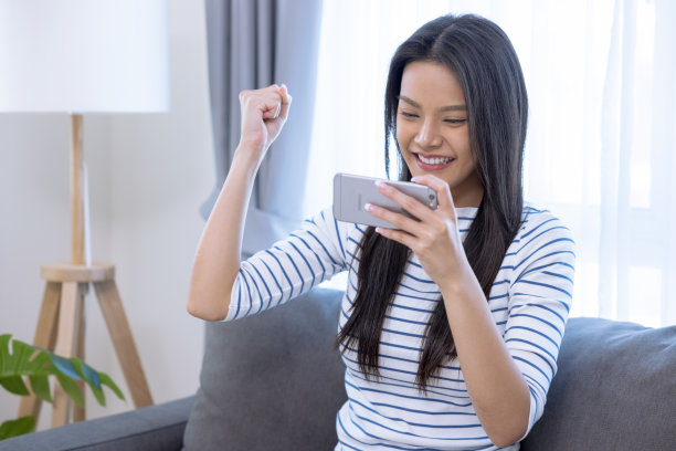 年轻的亚洲女性坐在家里的沙发上愉快地使用电话。图片 年轻的亚洲女性坐在家里的沙发上愉快地使用电话。图片下载