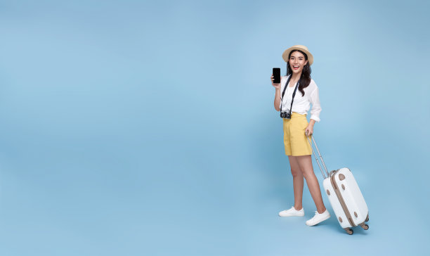 快乐的年轻亚洲旅游女性显示智能手机去旅行度假隔离在蓝色背景。图片 快乐的年轻亚洲旅游女性显示智能手机去旅行度假隔离在蓝色背景。图片下载