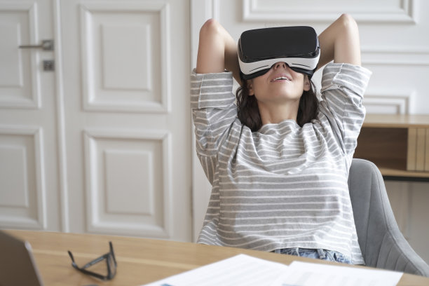 年轻快乐的女员工戴着VR眼镜在工作场所看电影图片 年轻快乐的女员工戴着VR眼镜在工作场所看电影图片下载