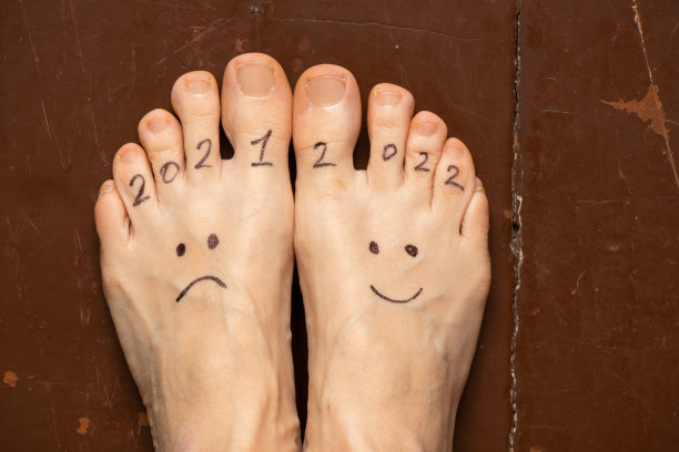 2021年和2022年忧伤和喜悦的笑脸画在一个女孩的腿上,在房子的木地板上,成功在2022年,快乐在新年图片 2021年和2022年忧伤和喜悦的笑脸画在一个女孩的腿上,在房子的木地板上,成功在2022年,快乐在新年图片下载