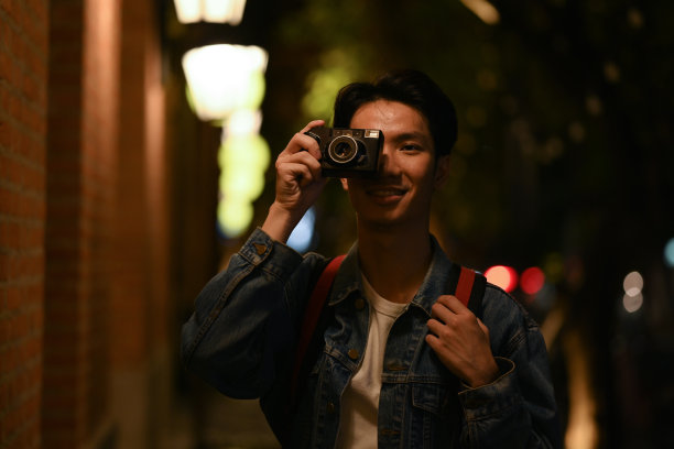 帅气的潮男用复古相机在城市中行走,模糊的夜间街灯背景。图片 帅气的潮男用复古相机在城市中行走,模糊的夜间街灯背景。图片下载