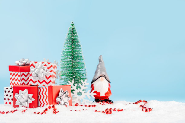 圣诞老人拿着装着新年礼物的盒子放在雪地上,旁边是一棵圣诞树,蓝色背景上有红色闪亮的珠子。新年贺卡。副本的空间。新年贺卡背景。圣诞家居装饰。图片 圣诞老人拿着装着新年礼物的盒子放在雪地上,旁边是一棵圣诞树,蓝色背景上有红色闪亮的珠子。新年贺卡。副本的空间。新年贺卡背景。圣诞家居装饰。图片下载