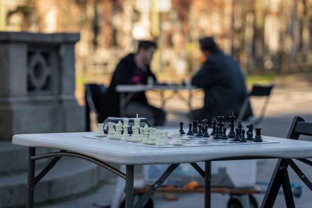 在街上的棋盘上准备下棋。背景模糊,棋手的剪影在桌子上。图片 在街上的棋盘上准备下棋。背景模糊,棋手的剪影在桌子上。图片下载