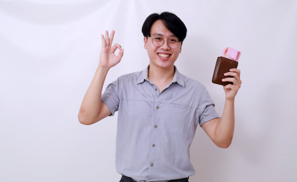 快乐的亚洲人拿着印尼钞票和钱包,同时做了一个不错的手势图片 快乐的亚洲人拿着印尼钞票和钱包,同时做了一个不错的手势图片下载