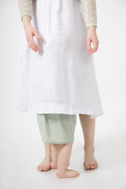 赤脚一家人站在白色背景上的裁剪照片。无法辨认的女人把小女孩藏在裙子里。图片 赤脚一家人站在白色背景上的裁剪照片。无法辨认的女人把小女孩藏在裙子里。图片下载