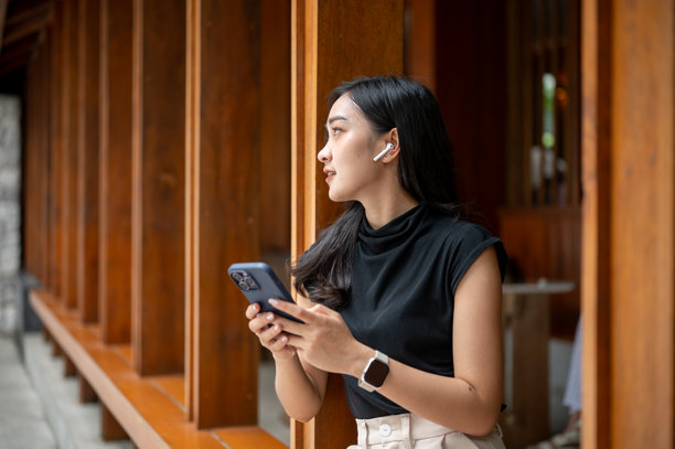 一位亚洲女性戴着耳机,在走廊里坐着,或在听音乐或在打电话,目光望向别处。图片 一位亚洲女性戴着耳机,在走廊里坐着,或在听音乐或在打电话,目光望向别处。图片下载