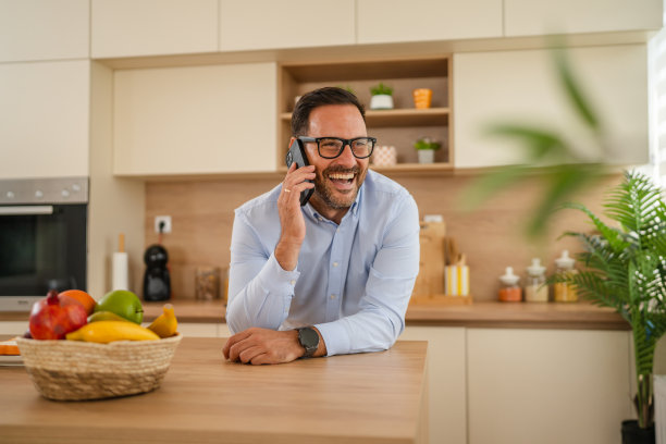快乐的男人在厨房里边打电话边微笑图片 快乐的男人在厨房里边打电话边微笑图片下载