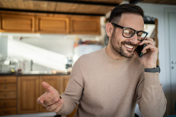 男人在家,边打电话边微笑并做手势图片 男人在家,边打电话边微笑并做手势图片下载