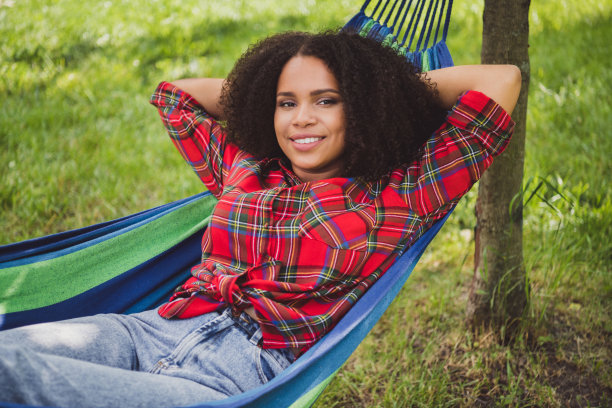 在城市公园的吊床上放松的女人肖像,她正在用智能手机打电话。图片 在城市公园的吊床上放松的女人肖像,她正在用智能手机打电话。图片下载