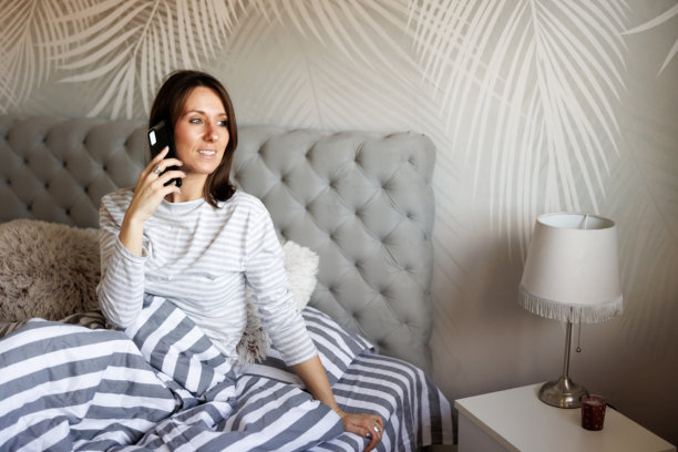 早晨醒来,女人在床上使用智能手机打电话。图片 早晨醒来,女人在床上使用智能手机打电话。图片下载