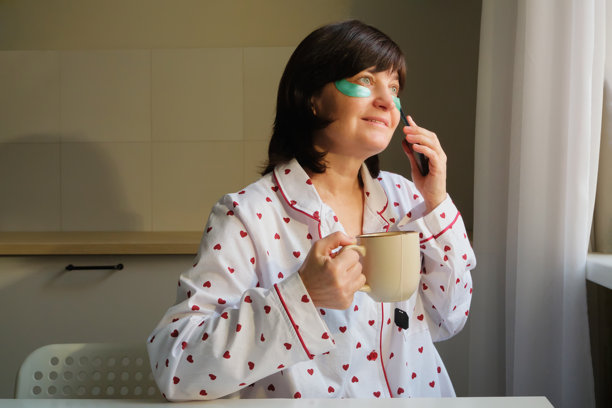 穿着睡衣和眼罩的女人在厨房喝咖啡并打电话图片 穿着睡衣和眼罩的女人在厨房喝咖啡并打电话图片下载